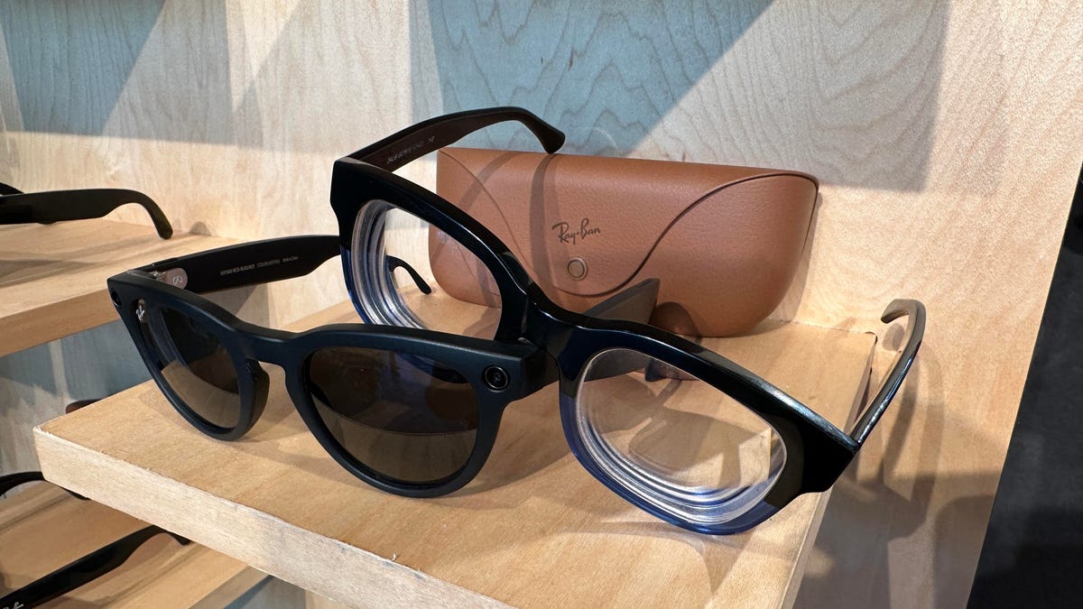 Two glasses resting on top of each other: one a pair of Ray-Ban smart glasses, the other regular blue and black glasses