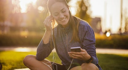 young woman sitting outside picking music for her workout