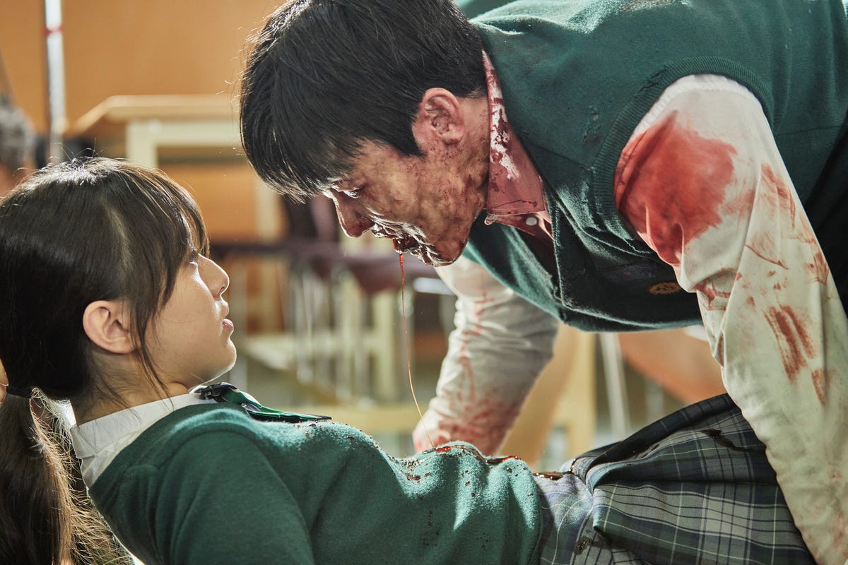 A bloodied zombie leans menacingly over a high-school student in a uniform.
