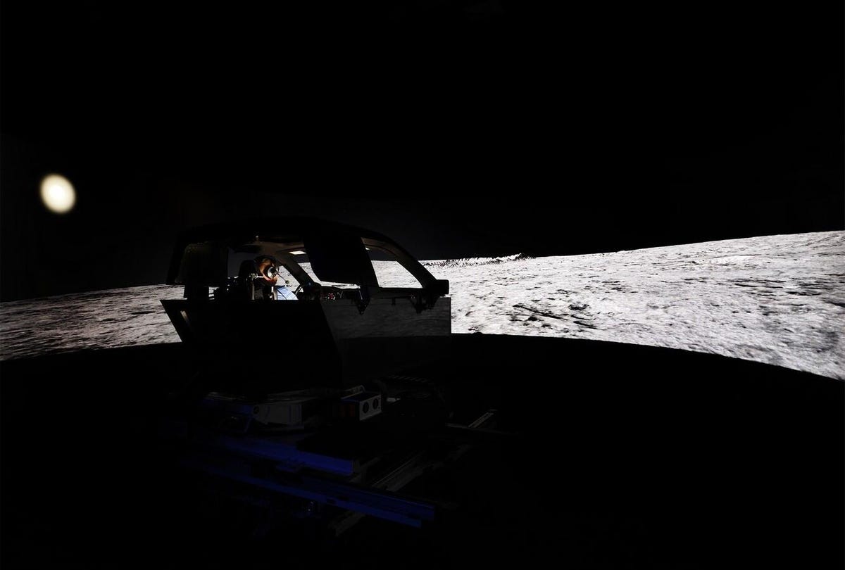 A silhouette of a driving simulator ahead of a projected image of the moon.