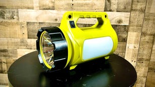 The LE Rechargeable LED Camping Lantern sits atop a black table in front of a wooden wall. It's a large-sized flashlight that doubles as a convenient lantern for camping trips.