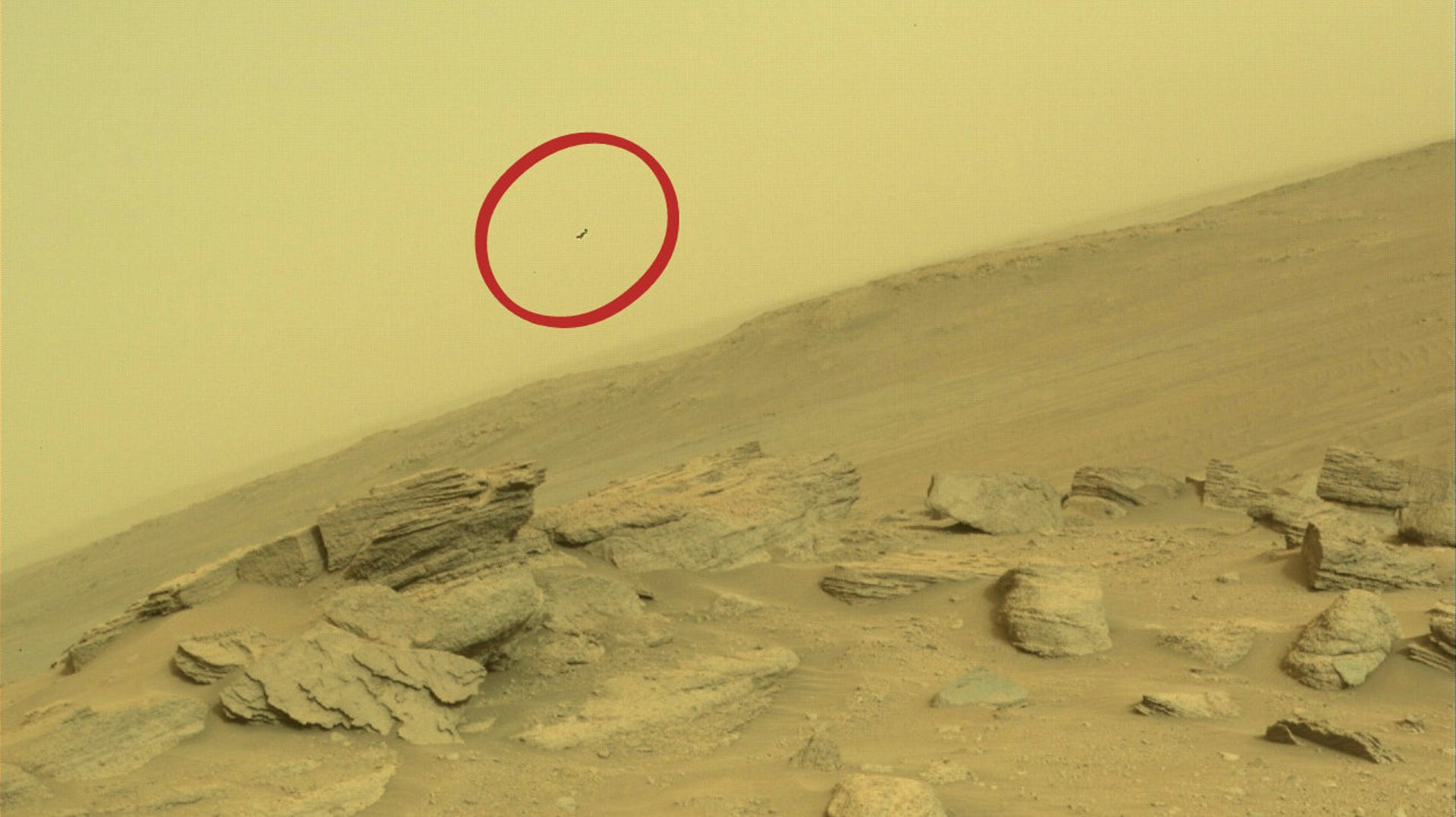 Rocky tilted Mars landscape with boulders shows a streak of something dark and small in the sky.