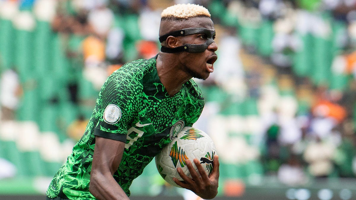El delantero nigeriano Victor Osimhen grita, lleva una mascarilla protectora y sostiene un balón bajo la mano izquierda.