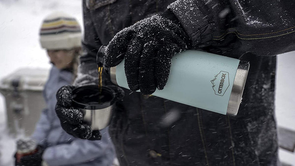 People in the snow use an OtterBox Elevation tumbler (28 ounce) to pour coffee into a cup.
