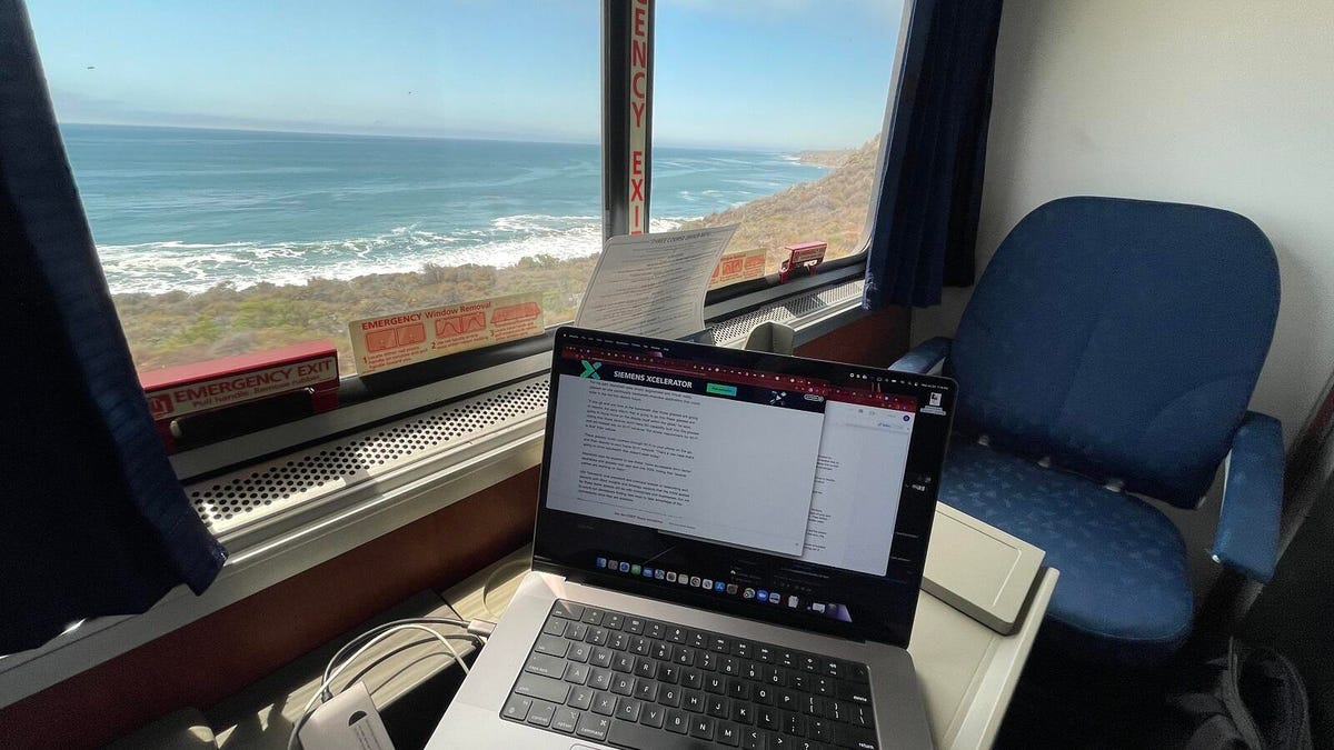 A view from inside a train's private room: a laptop the reporter's working on and a wide beach view speeding by the window.