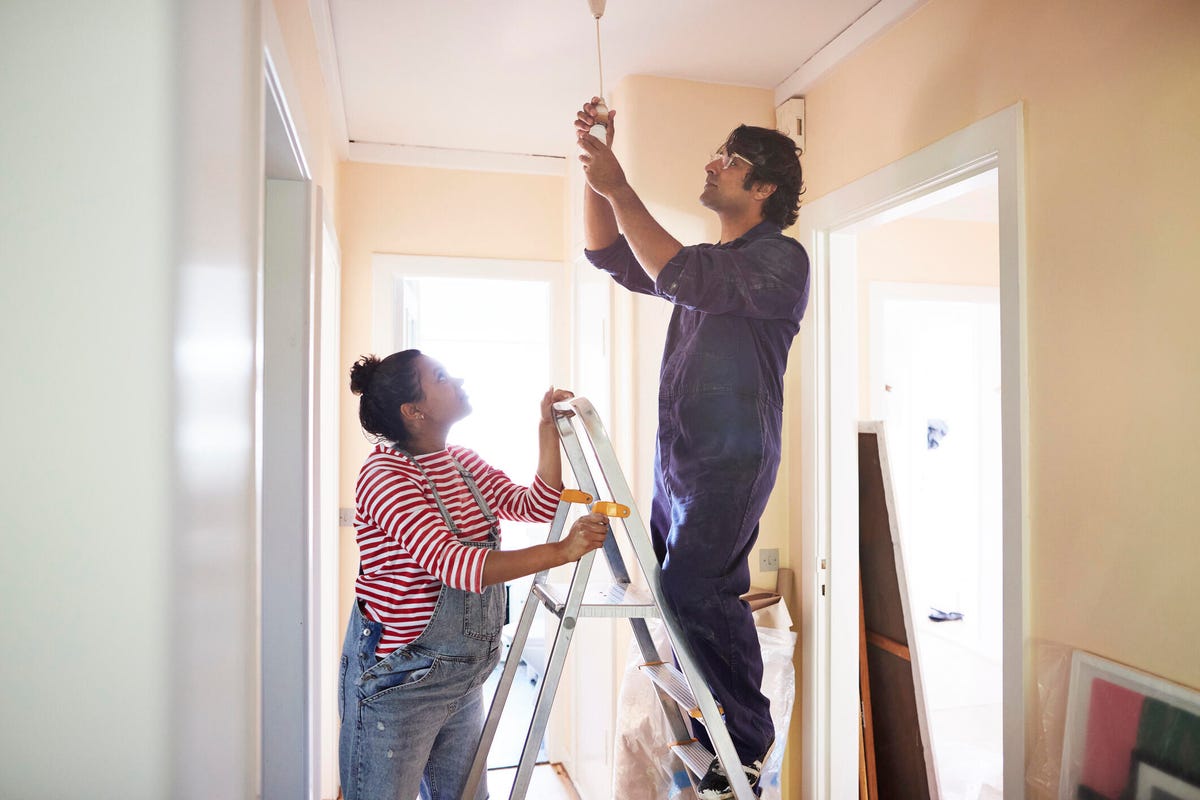 couple on ladder changing a lightbulb in a new home