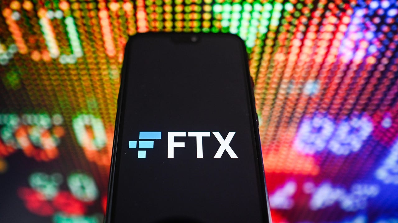 a phone with the FTX logo appears in front of a multicolored stock tracking board