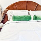 The Brooklinen comforter on a mattress with white and green pillows, and an orange headboard.