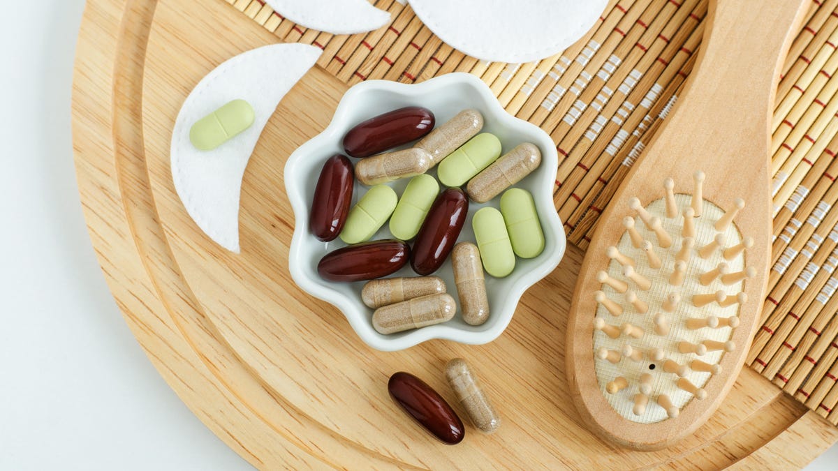 Small white bowl with food supplement capsules, pills and wooden hair brush.