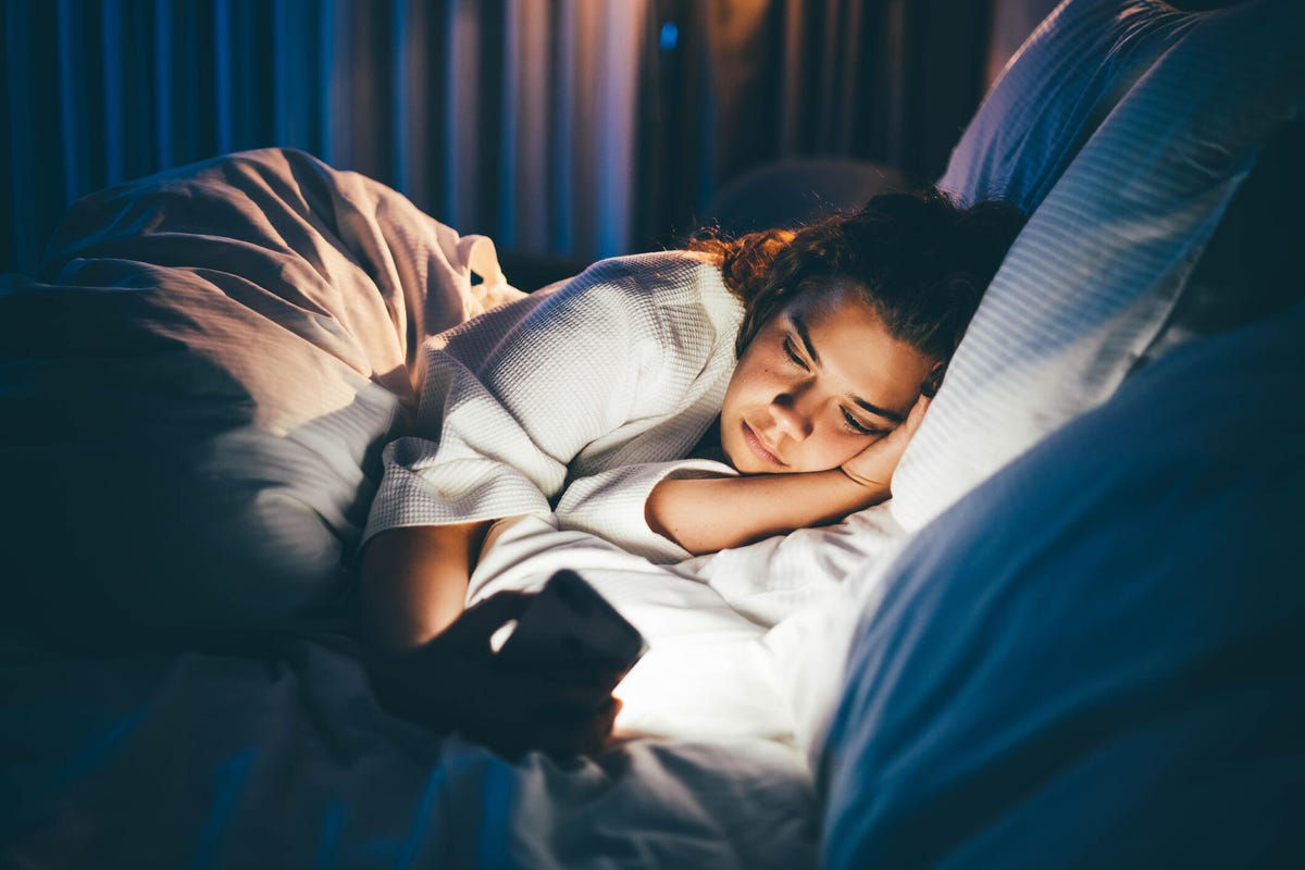 Young woman laying in bed and using smart phone.