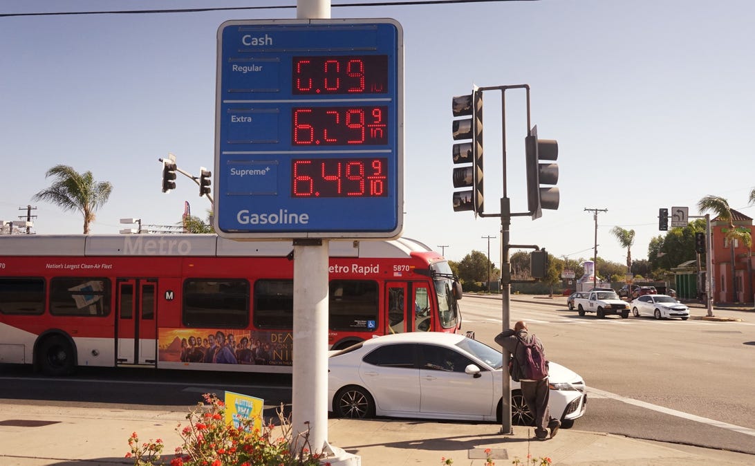 Gas prices on a sign at a station in Los Angeles country, with a car and a bus in the background