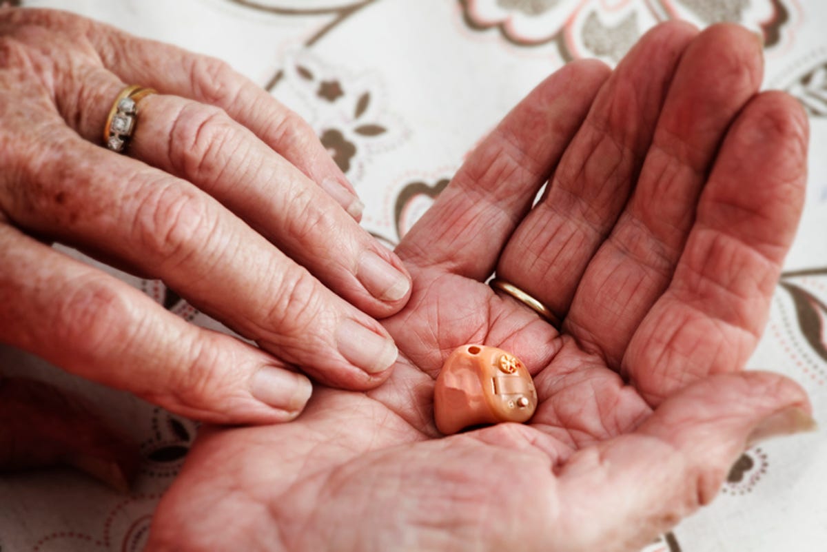 Older person holding in-ear hearing aid.