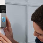 A woman uses a small screwdriver to install a Ring Video Doorbell on white trim.