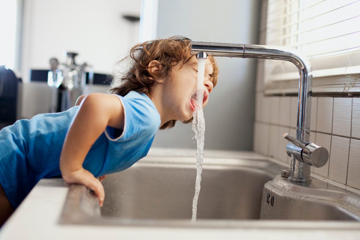 A young child drinking directly from the kitchen sink