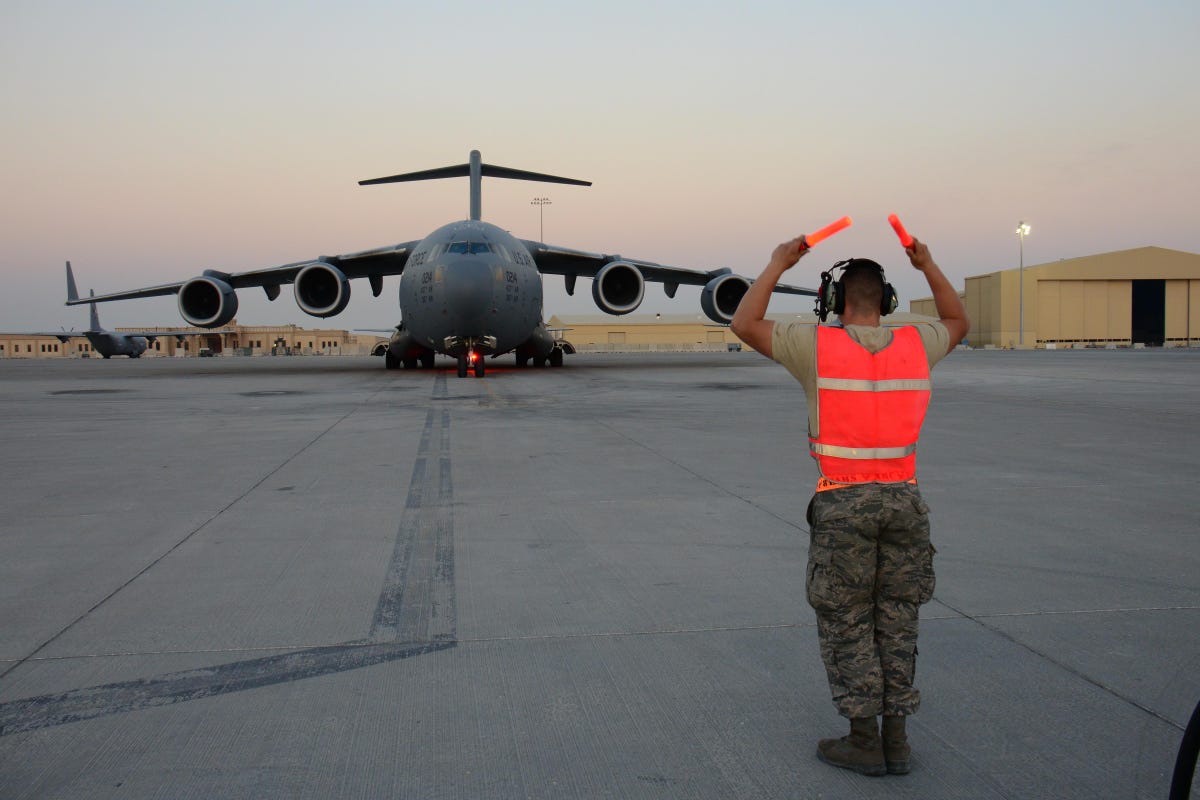 Boeing C-17 Globemaster III on a runway, with ground crew member signaling in the foreground