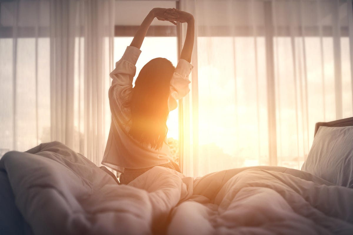 woman stretching in bed after waking up in the sunlight.