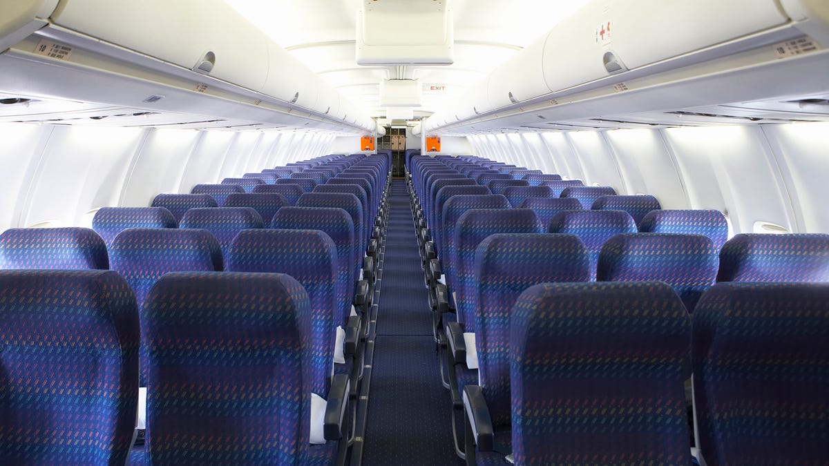 The inside of an empty commercial airliner, three blue seats on either side of the aisle.
