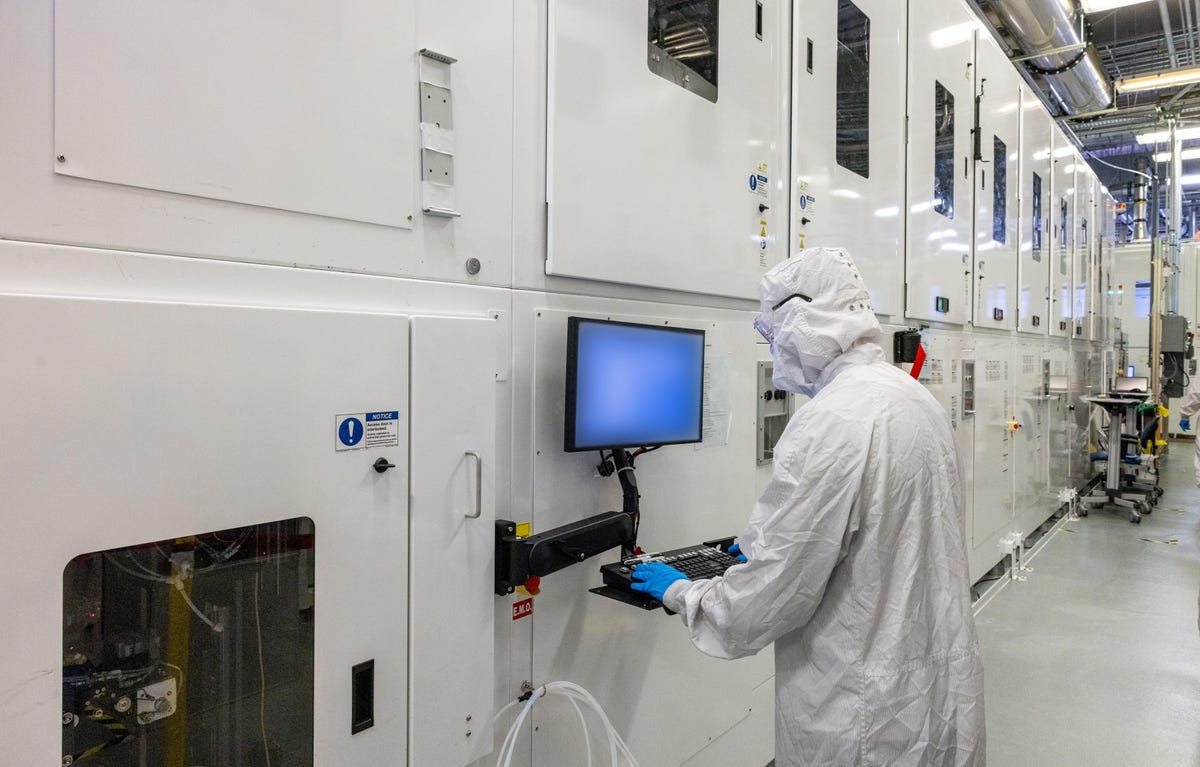 A two-story machine, sealed away from cleanroom air and longer than most buses, handles glass panels measuring 510x515mm that are transformed into complex multilayered rectangles for routing data and power to a processor.