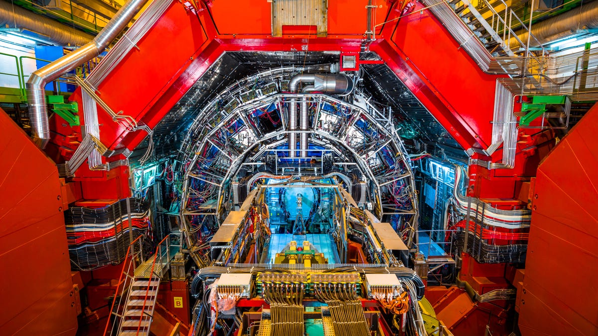 A large hexagonal red structure envelopes a smaller cylinder covered in wires and tubing at the Large Hadron Collider facility.