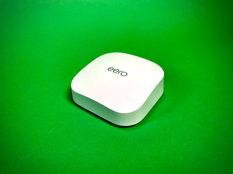 A single Eero Pro 6E mesh router sitting against a green background.