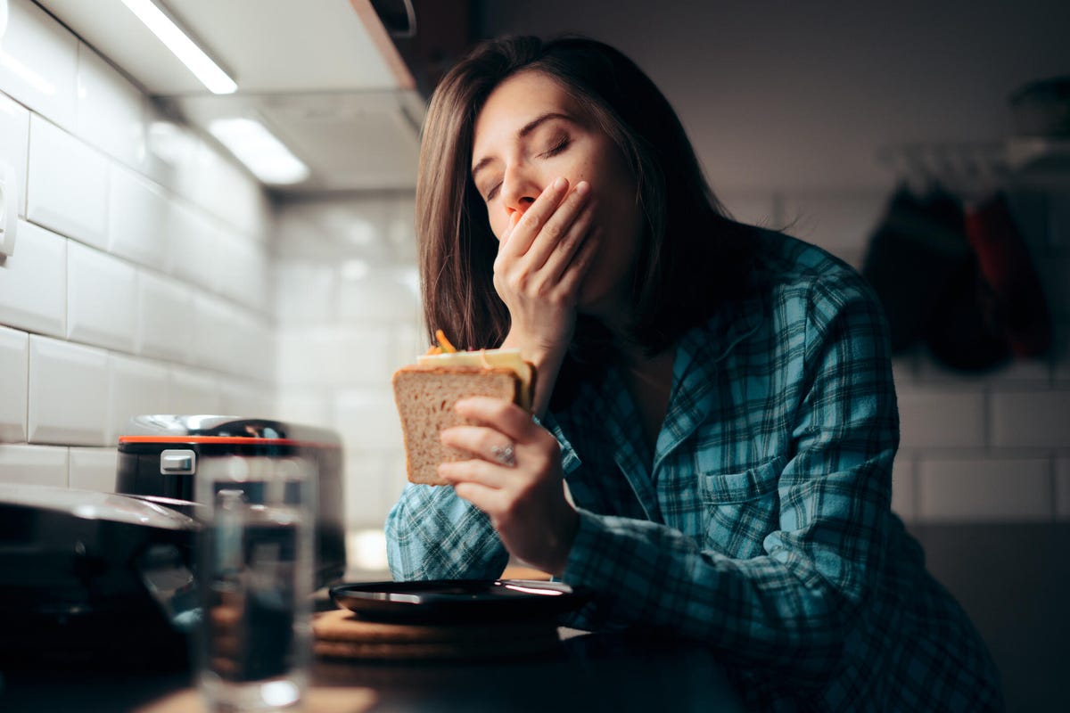 Sleepy woman eating a sandwich in her kitchen