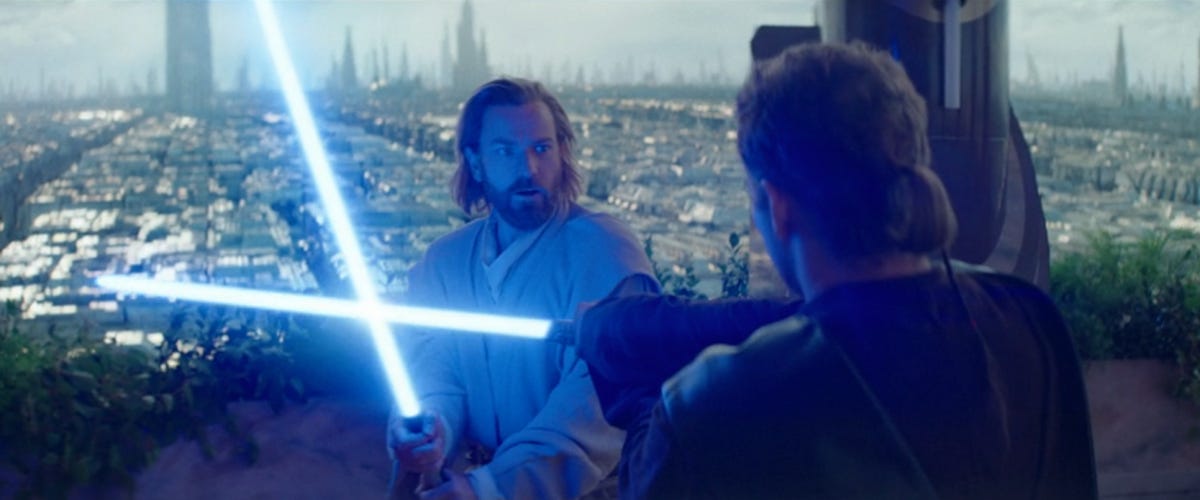 Obi-Wan Kenobi and Anakin Skywalker cross blue lightsaber blades in Obi-Wan Kenobi, with Obi-Wan facing the camera and Anakin with his back to us.