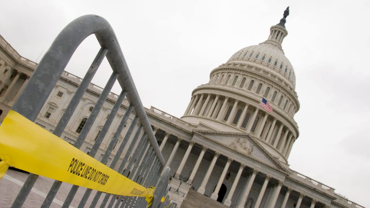 A fence with police tape sits outside the US Capitol on a cloudy, gray day