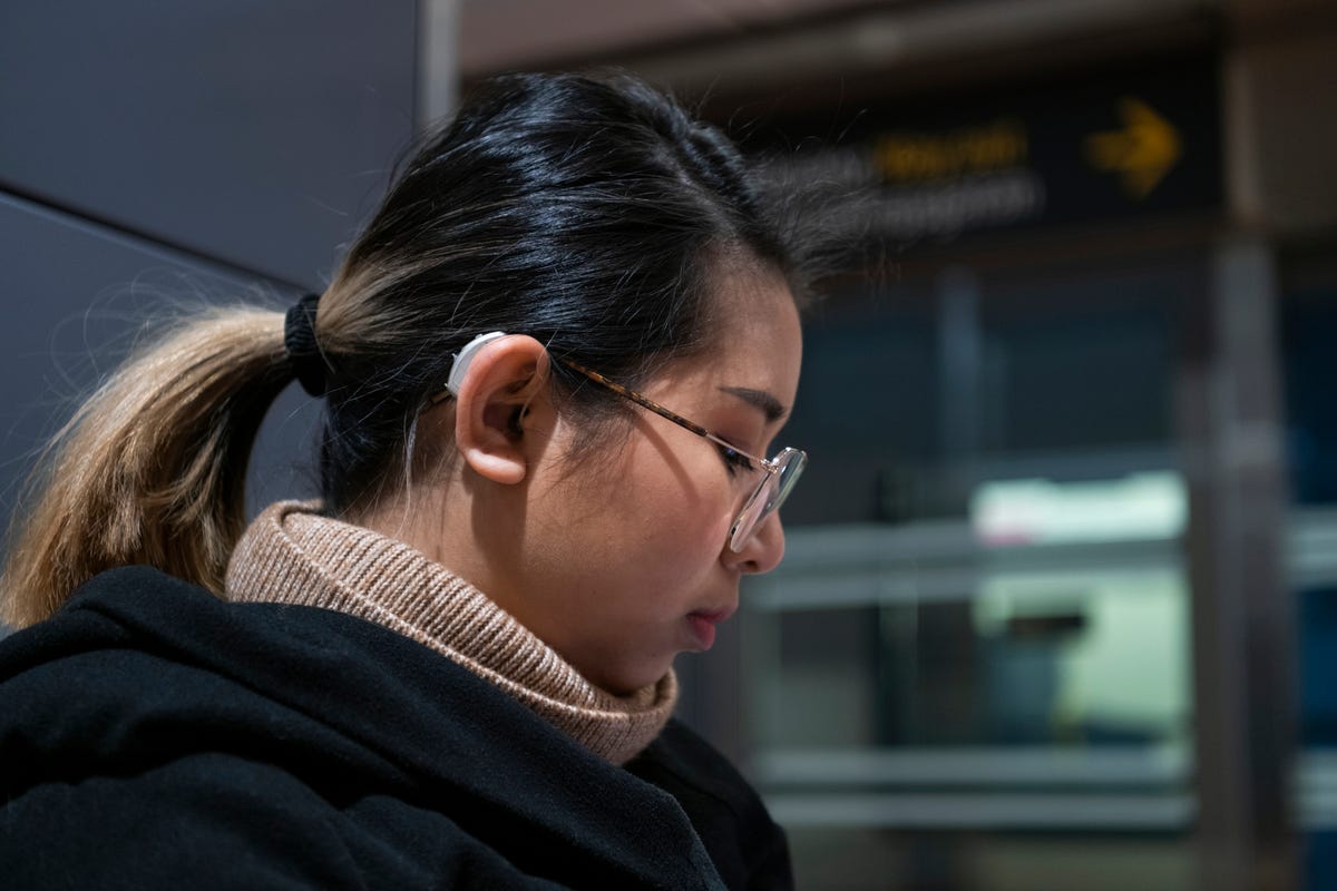 Young woman wearing glasses and a behind-ear hearing aid.