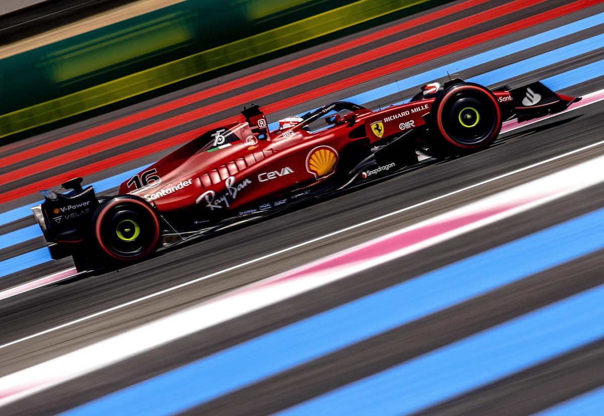A red Ferrari F1 car driven by Charles Leclerc races on a track covered in red, blue, and white lines.