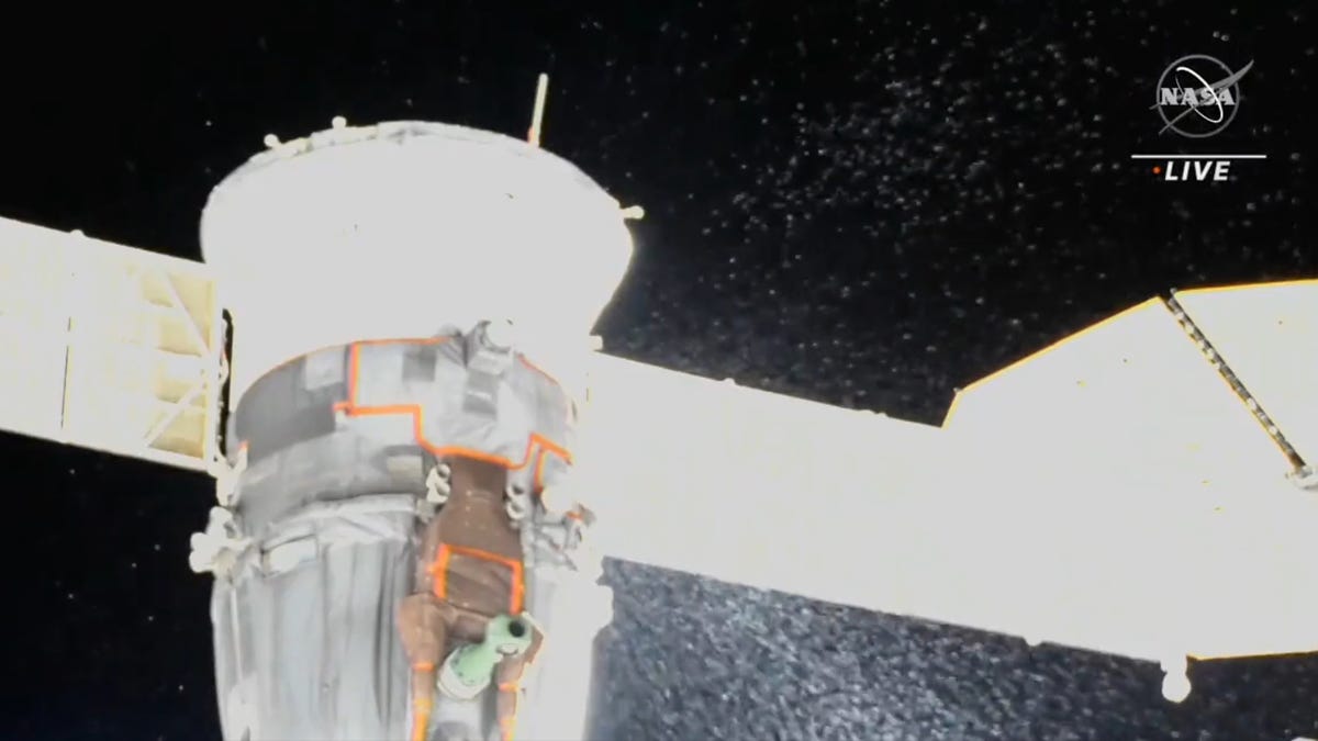 Screenshot of the Soyuz spacecraft docked to the ISS spewing coolant out into space in droplets.