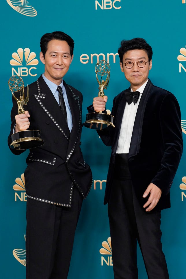Los dos hombres de traje negro sostienen un premio Emmy a la altura del pecho.
