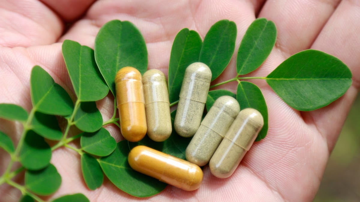 Supplements on top of a stem with leaves in someone's palm