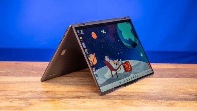 The 16-inch Lenovo Yoga 7i two-in-one laptop on a wooden table with a blue background.