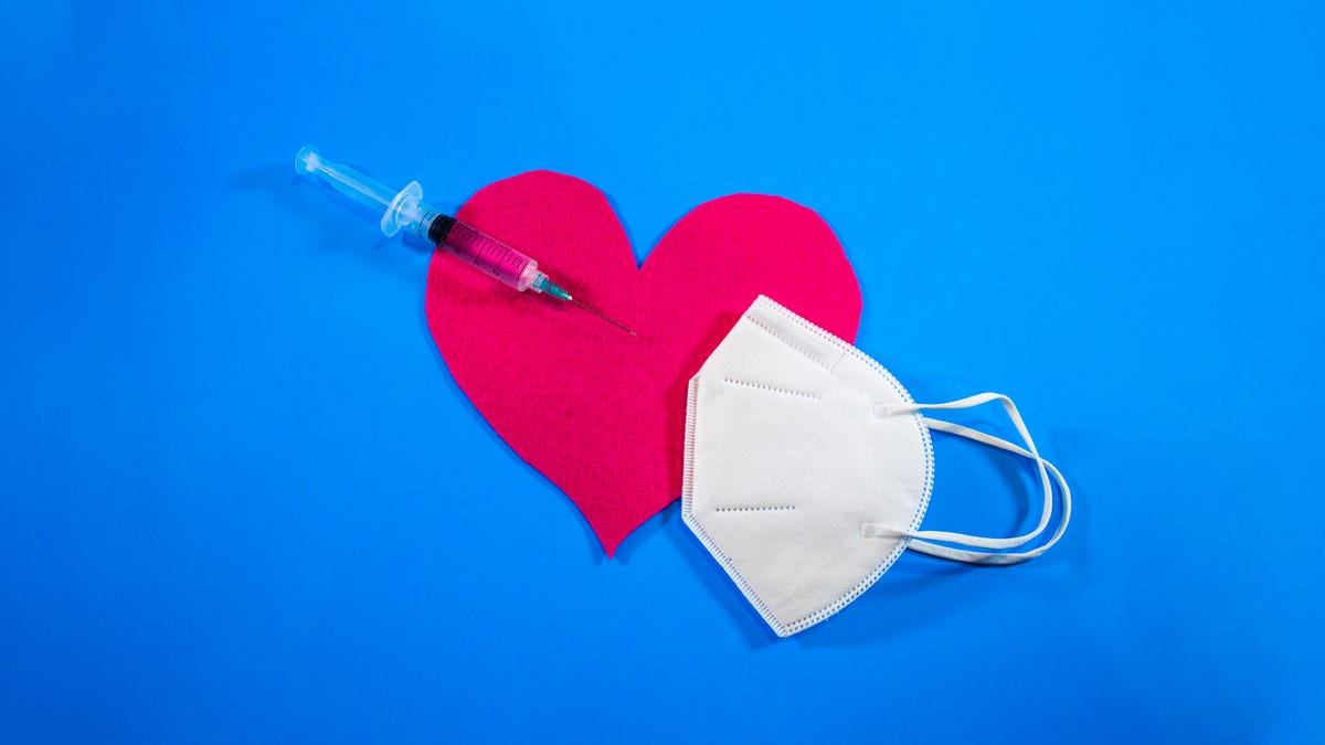A needle poked into a paper heart with a face mask just to the right