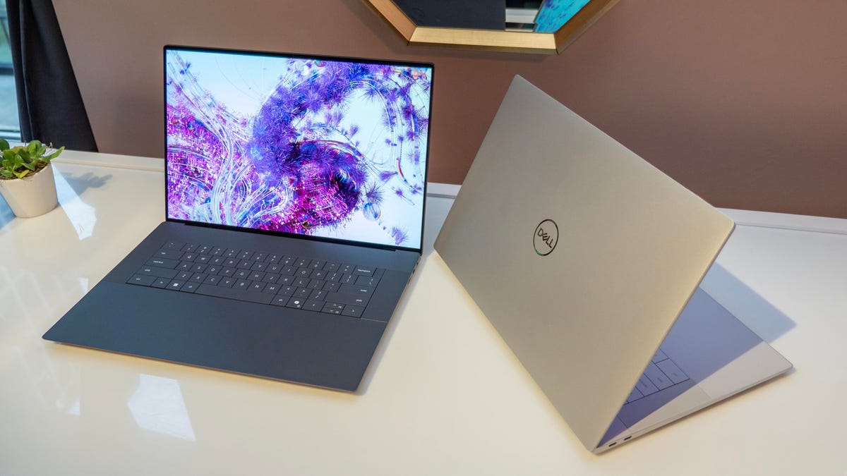 Dell XPS 16 in silver and gray sitting on a white glass table.