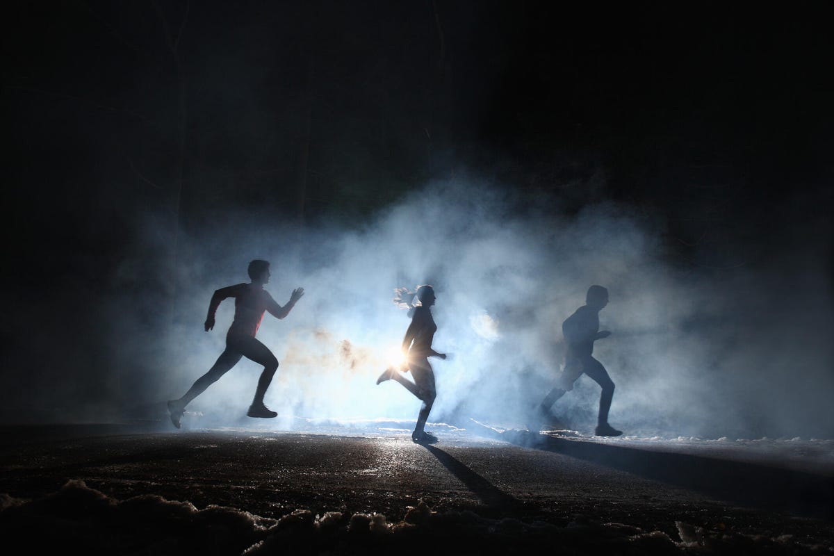 Three people running in the dark surrounded by illuminated mist