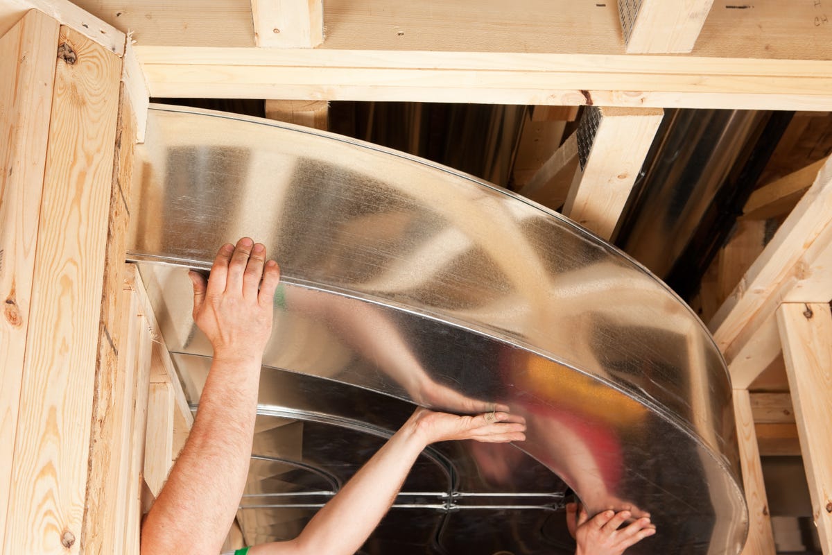 Hands holding air ducts in the framing of a house under construction