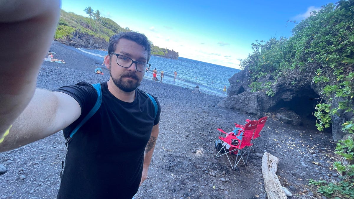 A man takes a selfie at an angle of him on the famous Wai'anapanapa Park's black sand beach.