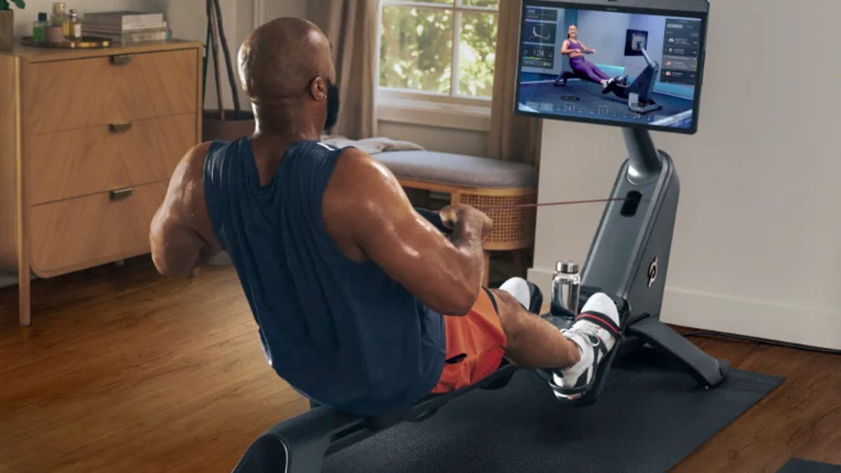 Man rowing at home and watching instructional video while using Peloton Row machine.
