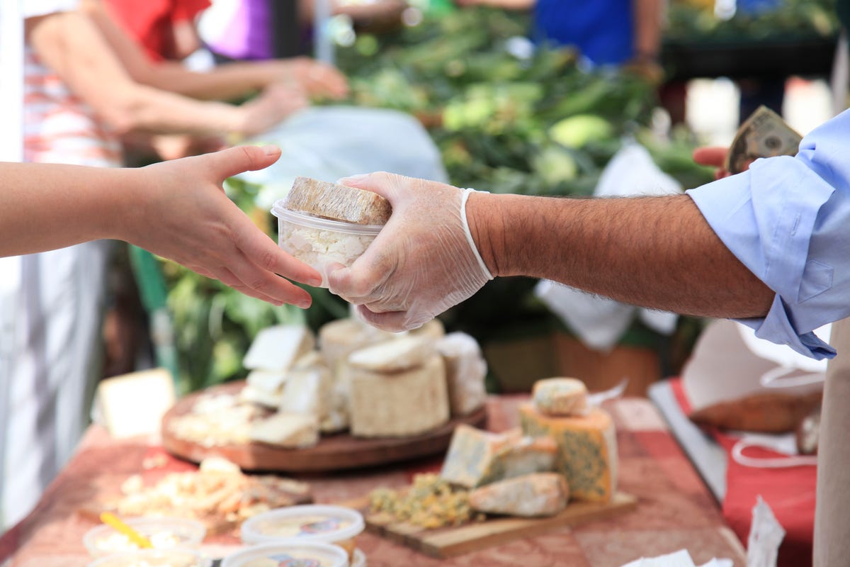 A cheesemonger handing a couple of packages of cheese to a customer at  market