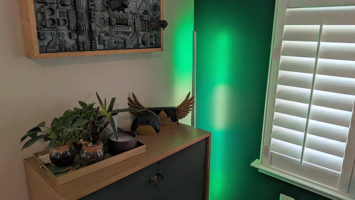 a green light glowing from a floor lamp next to a cupboard with plants on top