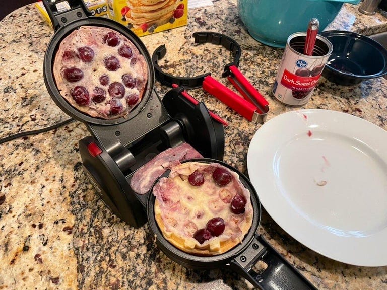 An open waffle maker with batter and fruits inside.