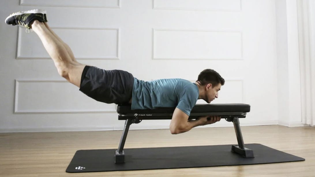 Man lies face down on Finer Form flat workout bench and lifts legs into the air.