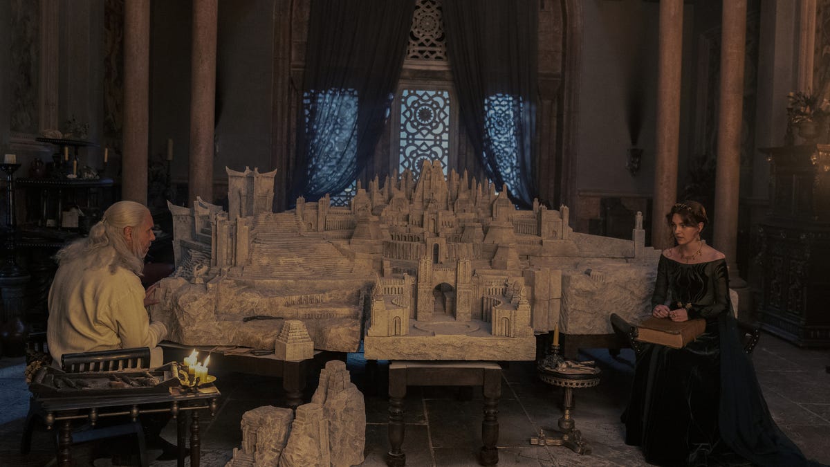 King Viserys and Alicent Hightower sit next to a large model sculpture of a sprawling castle