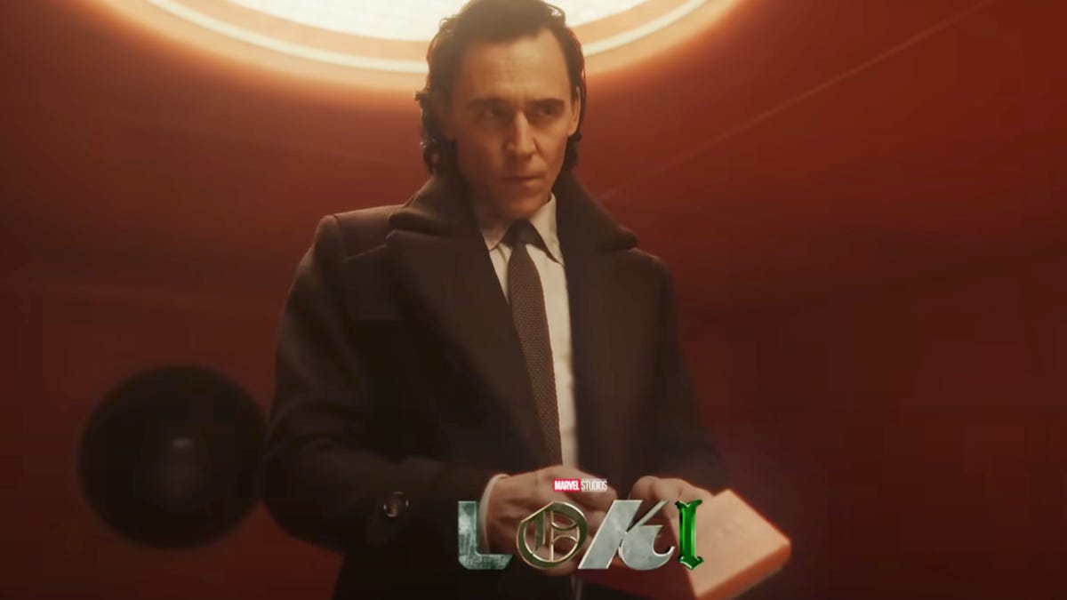 Loki standing in a dark red room