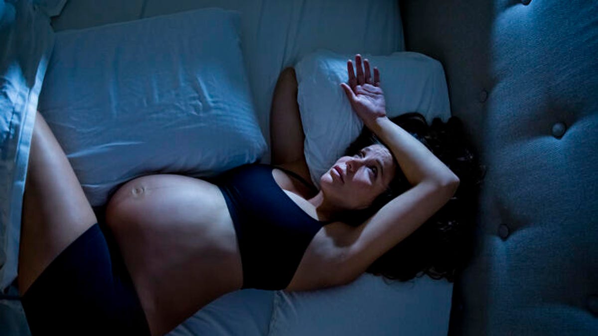 Pregnant woman lying down in bed but unable to fall asleep.