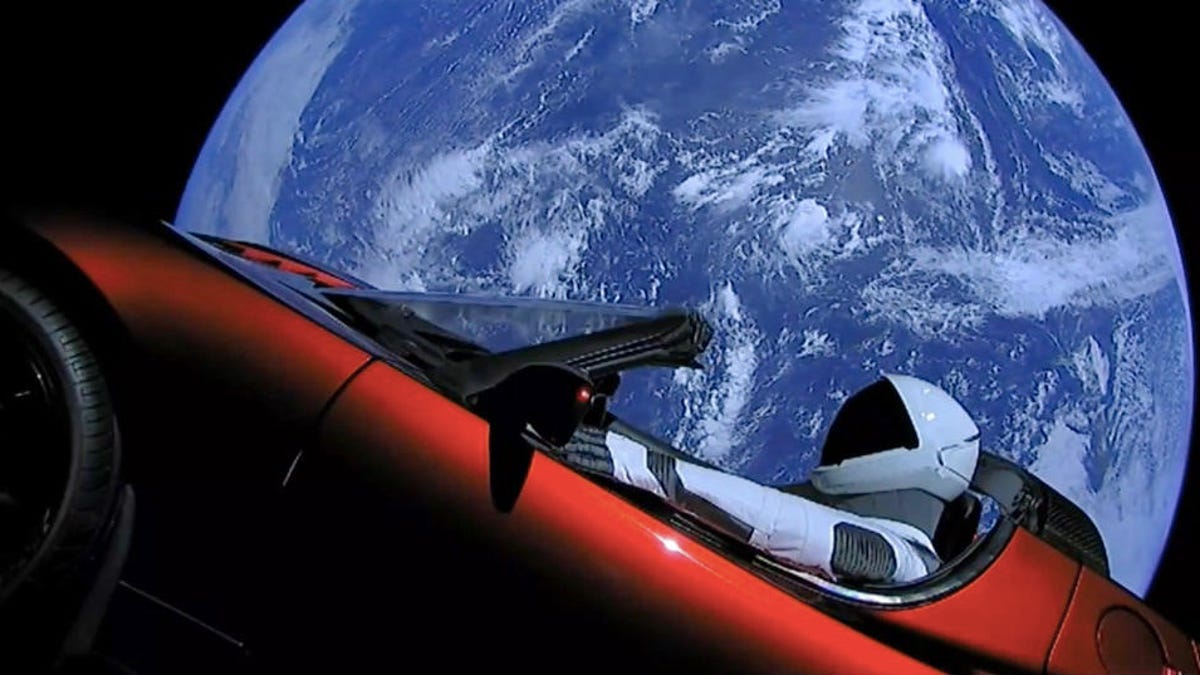 Red Tesla roadster seen at an angle with Earth behind it and helmeted Starman dummy at the wheel after launch in 2018.