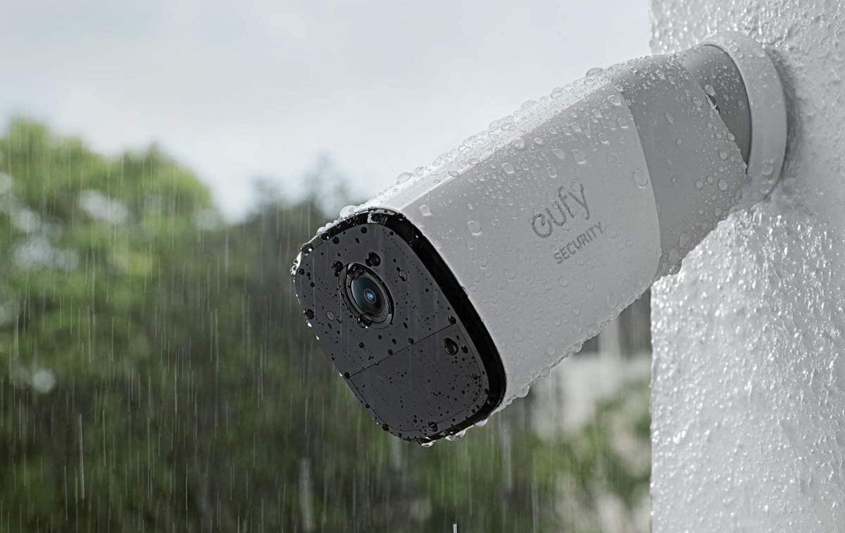 A white Eufy security camera mounted on an outdoor wall in the rain.
