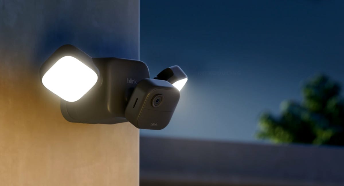 A Blink Outdoor 4 Floodlight Cam attached to the side of a home at dusk casts its 700 lumens of light into the yard.