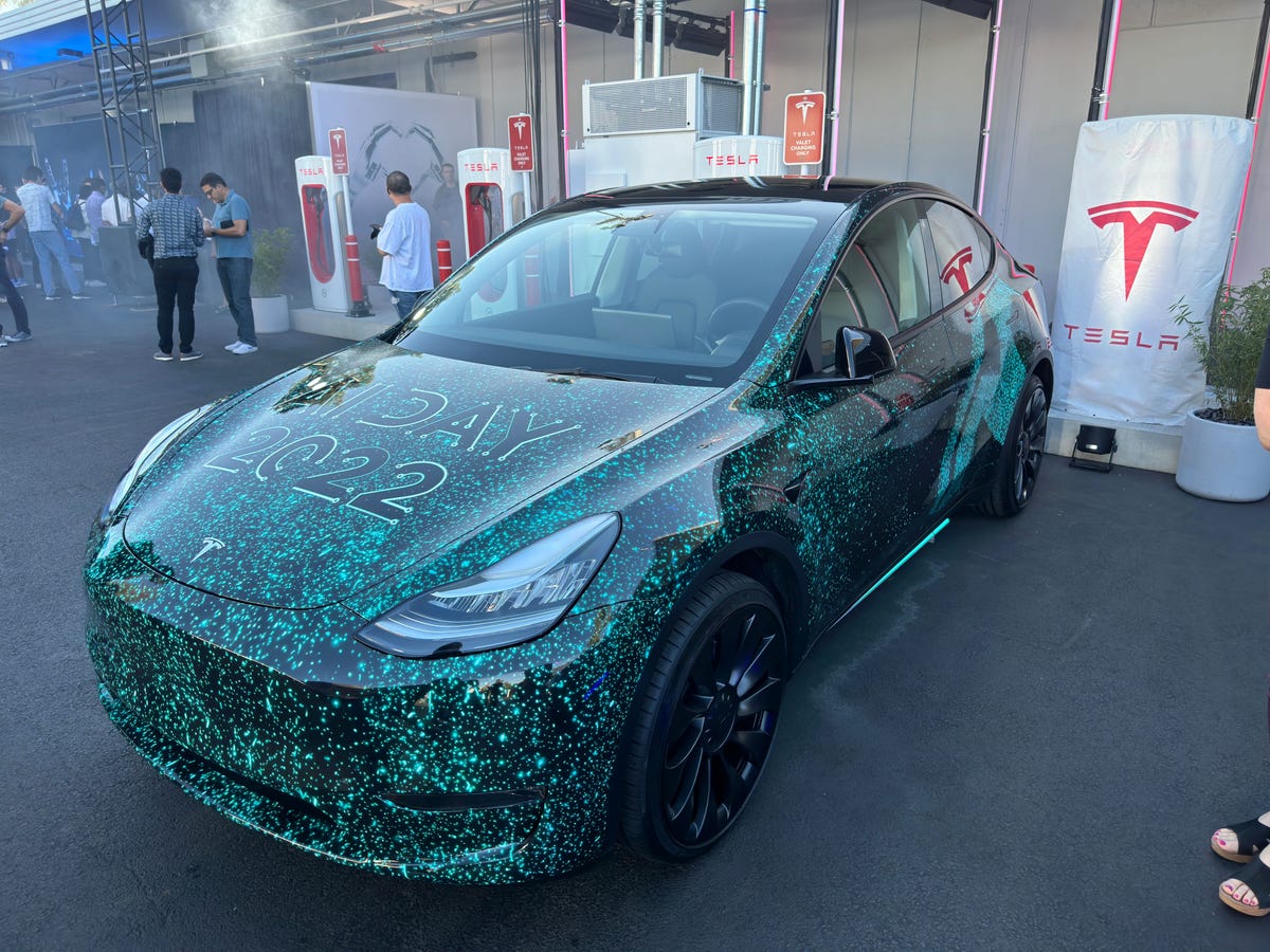 A Tesla electric car with a green Matrix-like paint scheme and "AI Day 2022" written on the hood.